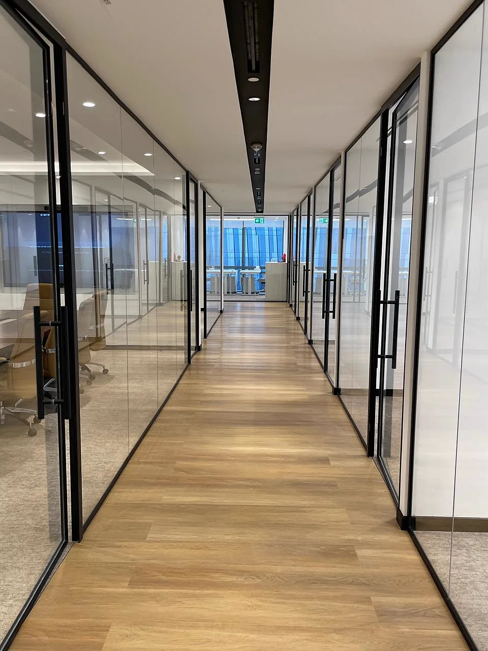 Black-framed glass office partitions lining a timber-floored corridor leading to a meeting area